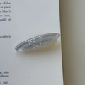 Close-up of a translucent grey resin hair clip with silver glitter and sequins on a book - Silver