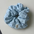 Close-up of light blue fabric scrunchie with black heart patterns and woven label - Blue Scrunchie