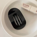 Detailed view of a black oval flat hair claw clip with unique vertical grid design on a plate - Glossy Black
