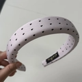Détail macro du serre-tête en satin rose rembourré avec motifs de cœurs noirs et étiquette - Serre-tête Rose