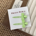 Detail view of two mint green bow hair clips on a white card board packaging - Green