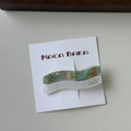 Detail of wavy acetate hair clips in marble green and glitter white on a display card - Green System