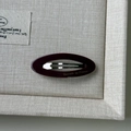 Vista macro della clip BB in resina bordeaux con scritte dorate su lino beige - Viola scuro