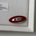 Dettaglio macro del fermaglio ovale rosso in acetato con scritte dorate Barrette la France - Rosso
