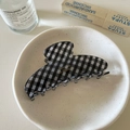 Detail view of a black and white checkered hair claw clip with golden text in a ceramic dish - Black Plaid Hair Claw