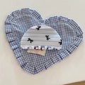Détail d'une pince à cheveux à rayures bleues et motifs nœuds sur coussin vichy - Demi-cercle Style