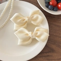Elegant pair of cream satin bow hair clips for women on a decorative ceramic plate - Off-white