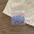 Close-up of four blue and white checkered hair clips in transparent packaging on wood - Navy Plaid
