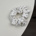 Gedetailleerd beeld van witte stoffen scrunchie met bloemenpatroon en een merklabel eraan - Klein Rijstwit