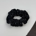 Close-up van de zwarte stoffen scrunchie met bloemenprint en een merklabel erop - Klein Zwart