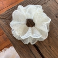 Detailopname van witte vierlaagse kant-scrunchie met borduursel op donker hout - Off-wit