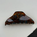 Detailed macro view of acetate hair claw clip featuring tortoiseshell pattern and gold text - Blue Brown Gradient