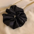 Détail d'un chouchou en satin noir avec un logo nœud blanc sur une étiquette en tissu noir - Noir
