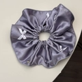Détail du chouchou en satin lilas avec petits nœuds blancs et breloque argentée - Violet