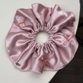 Détail d'un chouchou en satin rose avec petits nœuds et une plaque dorée élégante - Rose