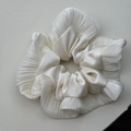 Détail d'un chouchou en satin blanc avec des bords à volants élégants et une texture brillante - Blanc Cassé