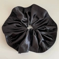Chouchou élégant en satin noir avec reflets soyeux et plis denses sur fond beige - Noir