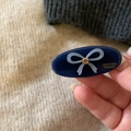 Dark blue oval hair clip with light blue bow and amber crystal detail in hand - Blue