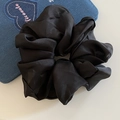 Detailed close-up of a black satin scrunchie featuring elegant glossy folds and texture - Black