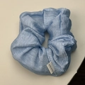 Detail of light blue wrinkled fabric scrunchie with a white Hand Made textile label - Blue Scrunchie