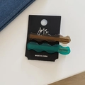 Détail de barrettes à cheveux ondulées en acétate marron et vert avec lettrage doré - Café Vert