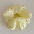 Detail shot of pale yellow scrunchie with pleated texture and a Hand Made woven label - Yellow