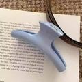Close-up of a matte light blue hair claw clip placed on an open book for styling details - Hanger Style