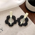 Gros plan de barrettes à fleurs noires à pois blancs sur un fond en tissu texturé - Style Fleur Noire