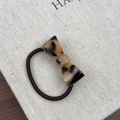 Detailed macro view of acetate tortoiseshell bow hair tie with engraved gold lettering - Light Leopard