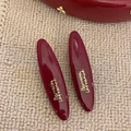 Detail of dark red oval hair clips with gold Barrette Lafrance script on beige fabric - Long Oval Style / Burgundy