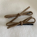 Detail of brown suede bow hair clips with black metal alligator base on white plush surface - Camel