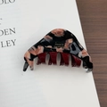 Detailed macro view of acetate hair claw clip showing marble pattern and handmade gold lettering - Black Brown