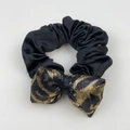 Detail of a black satin scrunchie paired with a golden leopard print bow hair accessory - Bow Hair Rope