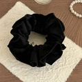 Detail van een zwarte fluwelen scrunchie met ruches op wit papier en houten achtergrond - Zwart
