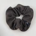 Close-up of soft knitted polka dot scrunchie in dark grey with a small ribbon logo tag - Hair Tie / Brown
