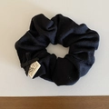 Detail eines schwarzen Strick-Scrunchies mit Seidenschleife und handgefertigtem Etikett - Schwarz