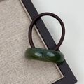 Detail of a dark green resin hair tie on a beige linen display tray with wood frame - Arc Green