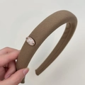 Detailed close-up of brown fabric padded headband with oval bow metal emblem in hand - Khaki