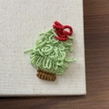 Close-up of a handmade knitted Christmas tree hair clip with a red bow and green yarn texture - Light Green Christmas Tree