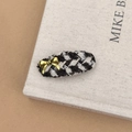 Macro d'une pince à cheveux à motif pied-de-poule avec un petit nœud doré élégant - Pince à Cheveux Ovale Noir