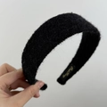 Dettaglio della texture in peluche nero e dell'etichetta dorata sulla fascia per capelli larga - Nero