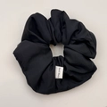 Detailed close-up of handmade black ruched scrunchie with satin texture and tag - Hair Tie / Black
