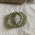 Detail of two translucent olive green spiral telephone wire hair ties on white fabric - Gradient Green
