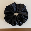 Close-up of a black satin scrunchie featuring a premium silk texture and woven brand label - Black