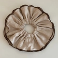 Detail eines champagnerfarbenen Satin-Scrunchie mit Seidentextur und Webkante - Khaki