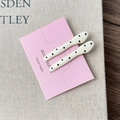 Close-up of elegant cream hair clips with black polka dots on a pink display card - Creamy White Textured Straight