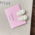 Detailed macro view of two cream hair clips with black polka dots on display card - Creamy White Textured Oval