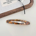 Detail of tortoiseshell acetate hair clip with silver metal spring closure on a white desk - Blue Brown Gradient