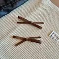 Close-up of two vintage brown leather bow hair clips on rustic woven fabric backdrop - Dark Coffee
