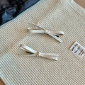 Detail of two beige faux leather bow hair clips with lychee grain and black duckbill grips - Off-white